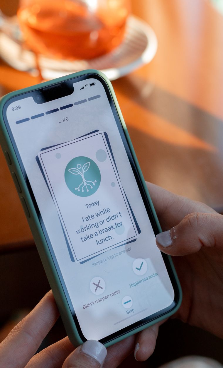 Hands hold a phone showing a card that reads: Today, I ate while working or didn't take a break for lunch. Buttons below say Didn't happen today, Happened today, and Skip.